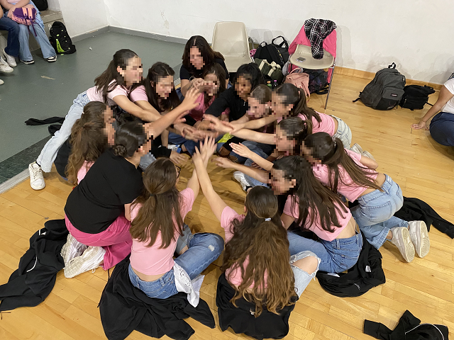Foto di gruppo con le studentesse che sedute in ginocchio in cerchio portano le mani in centro