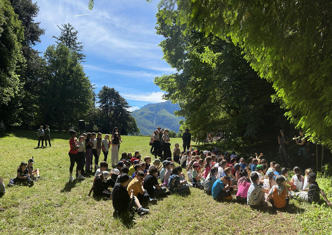 Bambini seduti in terra sul prato ascoltano due persone